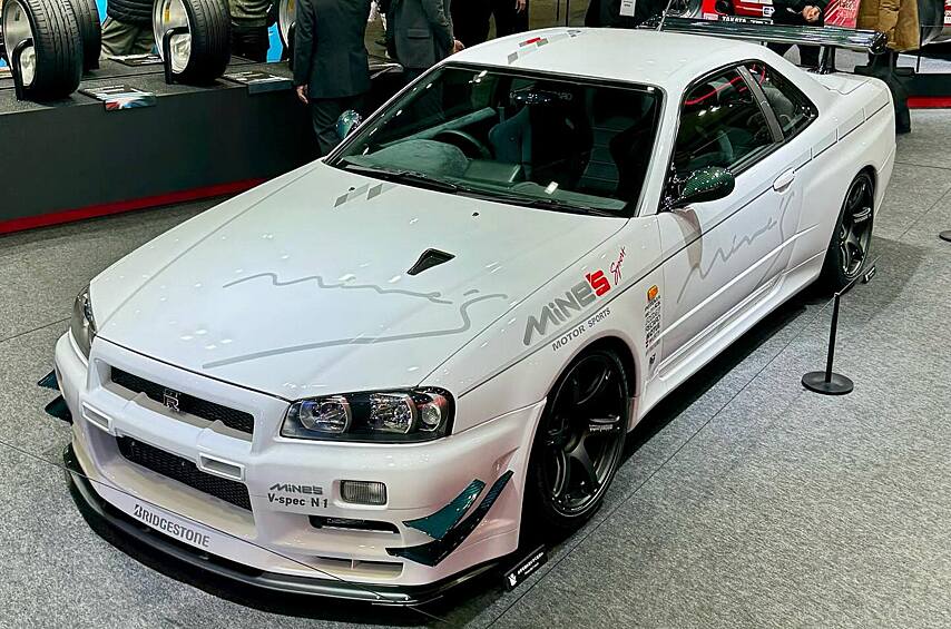 Не можем не отметить и вот этот Nissan Skyline GT-R (R34) в редком исполнении V-Spec N1. Это не просто кипенно-белый «скай» в декалях легендарной тюнинг-мастерской Mine's Sport, а очень качественный рестомод фирмы Built by Legends. Компанию организовали в 2018 году единомышленники Масахару Кудзи и Катсу Такахаши. Все их машины делаются по близкому рецепту. Кузов разбирают до голого металла и восстанавливают — у «скайлайнов» масса проблем с коррозией. Этим занимается известный Garage Yoshida, наладивший производство новых деталей — в частности, опорных стаканов передней подвески изменённой конструкции (родные детали гниют даже на ухоженных машинах). Часть кузовных деталей заменяют углепластиковыми копиями, но внешне стараются сохранить сдержанный стиль: например, на этой машине углепластиковый бампер и капот никак не отличаются внешне от штатных. Салон обшивают высококачественной искусственной замшей Ultrasuede. Под капотом — зона ответственности мастеров фирмы Mine's: установлен построенный ими двигатель RB28 сравнительно умеренной мощности (около 600 л.с.). Такая машина «под ключ» стоит около полумиллиона долларов.